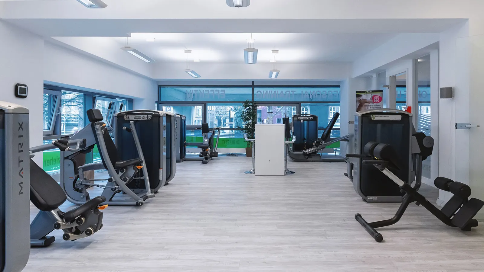 Heller Trainingsbereich mit Kraftgeräten und großen Fenstern